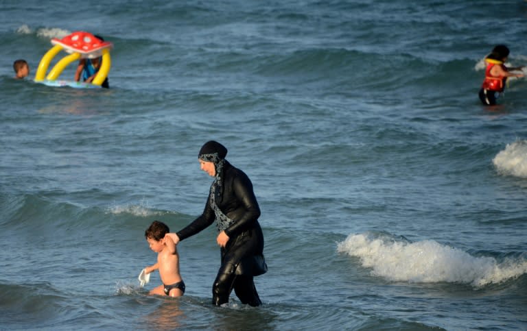 A Tunisian woman wearing a "burkini", a full-body swimsuit designed for Muslim women, walks in the water with a child on August 16, 2016 at Ghar El Melh beach near Bizerte, north-east of the capital Tunis