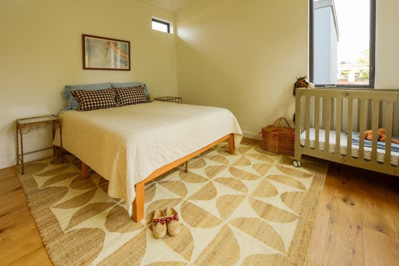 View of bed and crib in neutral toned bedroom.