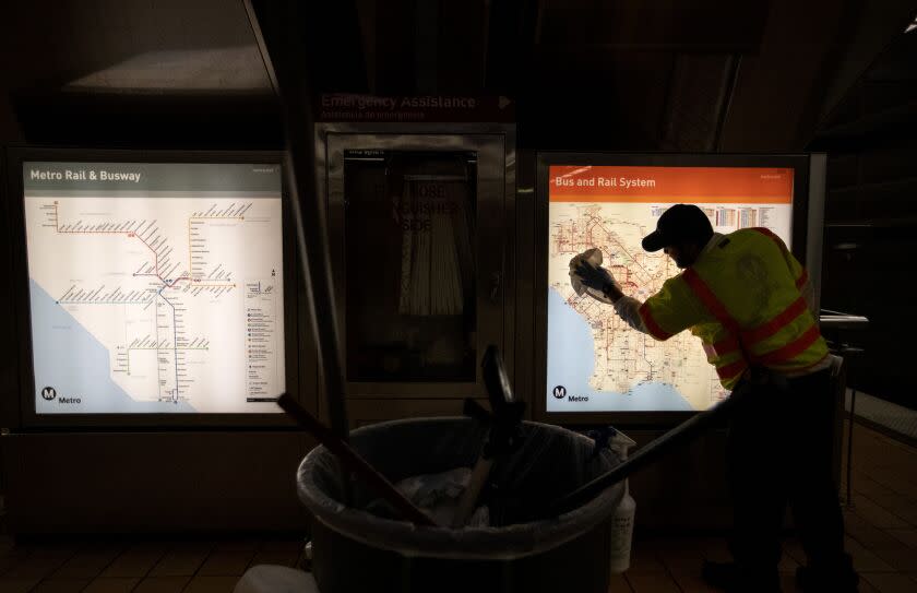 NORTH HOLLYWOOD, CALIF. -- THURSDAY, MARCH 26, 2020: A LA Metro custodian cleans a transit map inside the Metro Red Line's North Hollywood station in North Hollywood, Calif., on March 26, 2020. Metro has strengthened its cleaning regimes of buses, trains and facilities in the face of the coronavirus pandemic. (Brian van der Brug / Los Angeles Times)