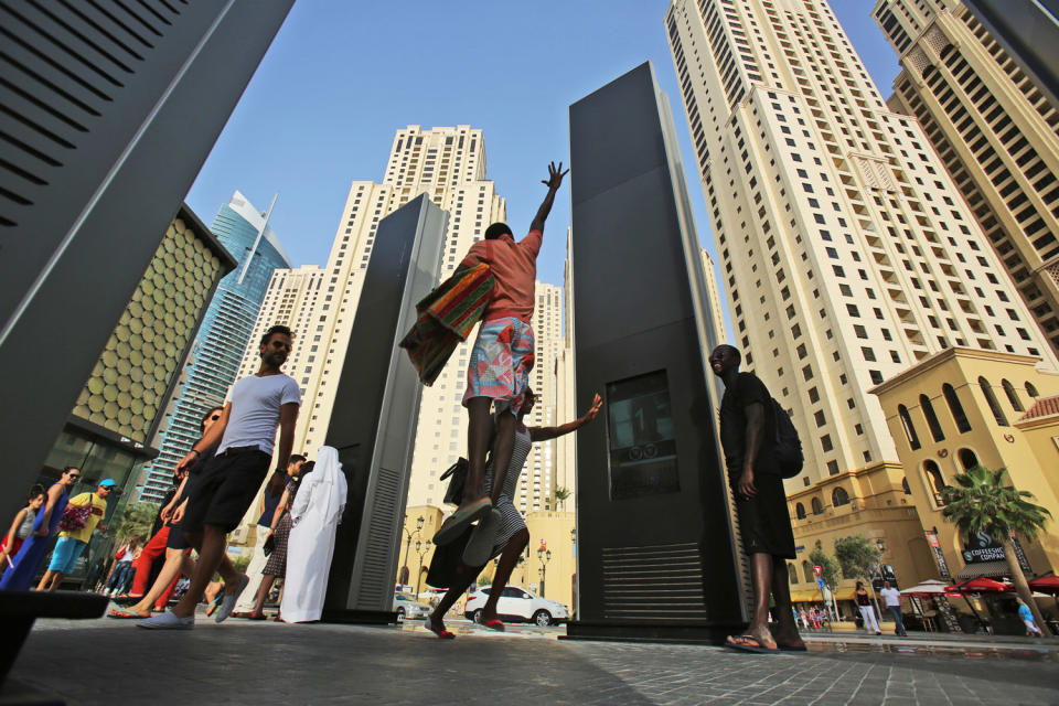 In this Saturday, April 19, 2014 photo, people try to get their picture taken from a camera installed on an advertising board at the entrance of the beach in Dubai, United Arab Emirates. The ribbon of beach nestled along the towering skyscrapers rising from Dubai’s man-made marina district is a rare spot in the Middle East, bringing together the conservatively dressed and the bikini-clad in a multiethnic mix of those with means and those still striving for a more comfortable life. (AP Photo/Kamran Jebreili)