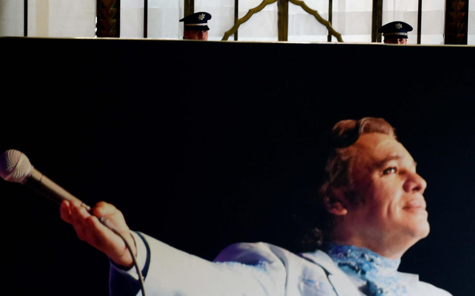 Police officers stand behind a poster of Mexico's late Latin music legend Juan Gabriel as the urn with his remains is displayed at Mexico City's ornate Palace of Fine Arts.