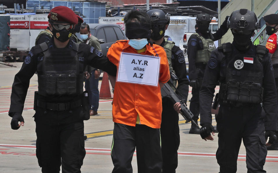 Police escort a suspected militant upon arrival at the Soekarno-Hatta International Airport in Tangerang, Indonesia, Thursday, March 18, 2021. Indonesian authorities on Thursday transferred suspected militants arrested in raids in the last few weeks, from East Java to the capital city for further questioning. The militants are believed to be connected to linked to the al-Qaida-linked Jemaah Islamiyah extremist group. (AP Photo/Achmad Ibrahim)