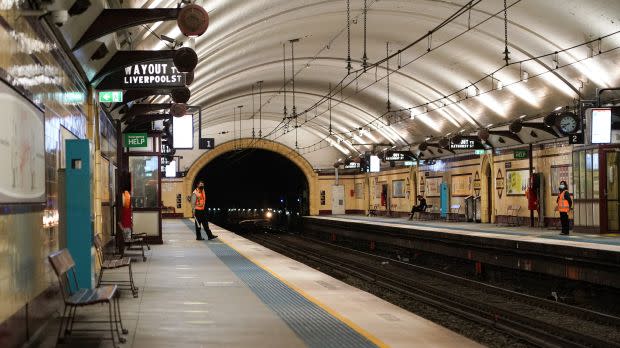 a subway train station in Sydney Australia is nearly deserted except for two workers wearing orange safety vests and masks