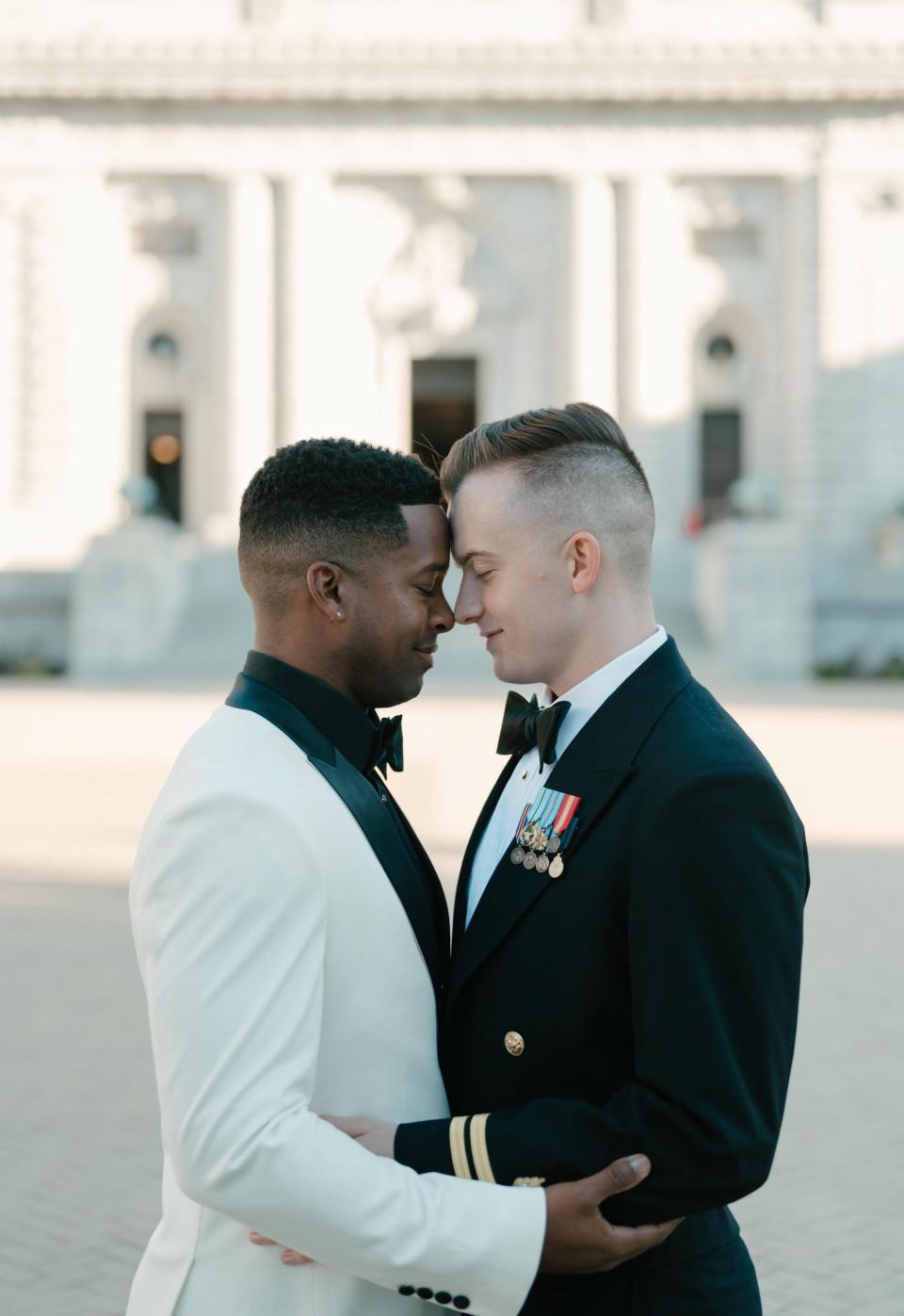 Two grooms lean their heads together in a courtyard.