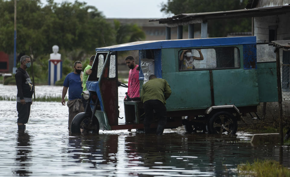 People try to start a stalled vehicle to transport people through a street flooded by rain brought on by Hurricane Ida, in Guanimar, Artemisa province, Cuba, Saturday Aug. 28, 2021. (AP Photo/Ramon Espinosa)