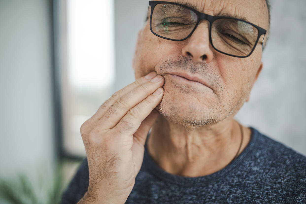 Senior male holding his cheek in pain, experiencing tooth ache