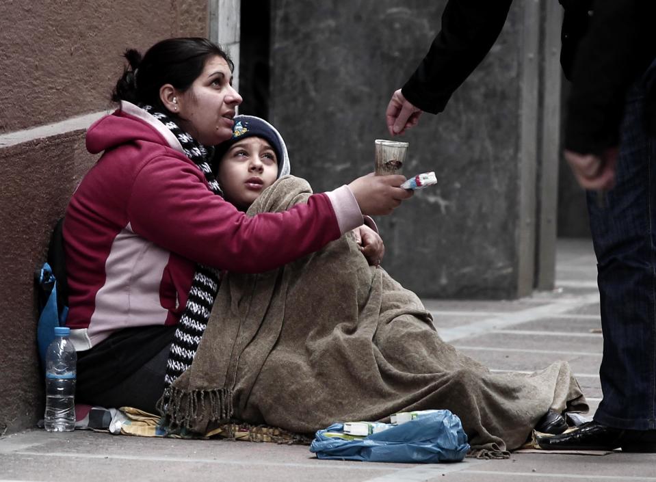 A woman holding a child begs for alms in central Athens, on Wednesday, Feb. 29, 2012. Late Tuesday, parliament approved new cuts in public sector pensions and government spending required to secure a second package of international rescue loans, while the Cabinet formally imposed deep cuts to the minimum wage, retroactively to Feb. 14. (AP Photo/Dimitri Messinis)