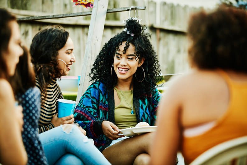 A group of friends sitting outside with plates and glasses in their hands.