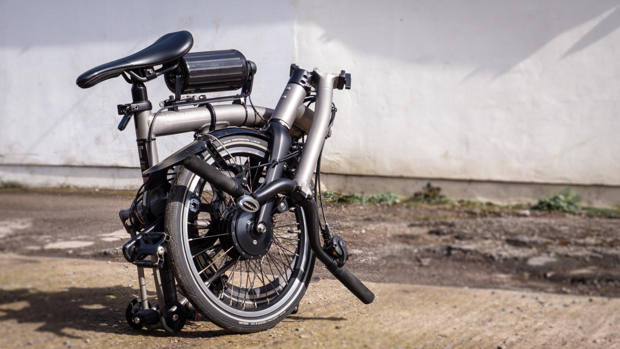  A black and silver folded Brompton T-Line, upgraded with the Cytronex e-bike conversion kit, sits on a rocky surface 