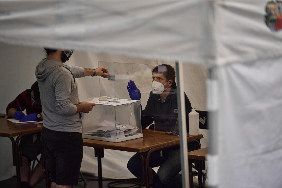 A resident shows his national identity card to a staff member of a polling station, while wearing face mask to help curb the spread of the coronavirus during the Basque regional election in the village of Ordizia, northern Spain, Sunday, July 12, 2020. Basque authorities are displaying special rules and practices in the protection against the coronavirus. (AP Photo/Alvaro Barrientos)