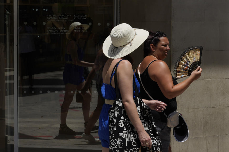 A tourist uses a fan to keep cool as she walks at Ledras street in downtown Nicosia, Cyprus, Thursday, July 13, 2023. The Meteorological Department said the heatwave's highest temperatures are expected July 14-15 when they're expected to reach 42-43 degrees Celsius inland and 34-36 degrees in the island's main Troodos mountain range. (AP Photo/Petros Karadjias)