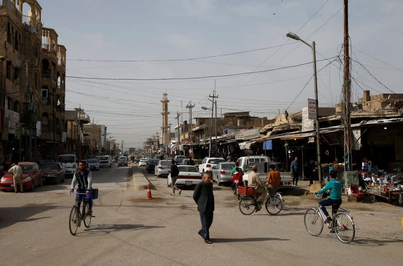 A man walks as others ride bicycles on a street in Falluja