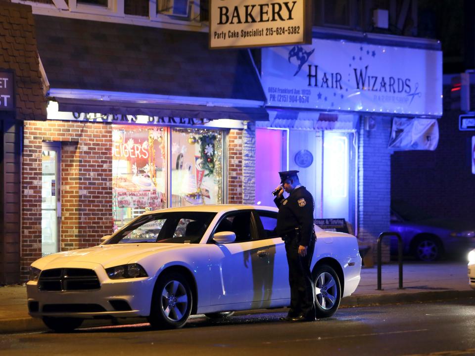 A police officer looks over a car in the Mayfair section of Philadelphia, Monday Dec. 15, 2014, that was being driven by a man who police shot and killed. Philadelphia police say an officer shot and killed the motorist who struggled with him and another officer during an early morning traffic stop.