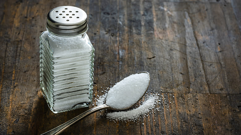Salt shaker with spoon of salt on wooden background
