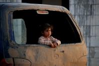 An internally displaced Syrian girl inspects the area from a broken window of a van in an IDP camp located near Idlib