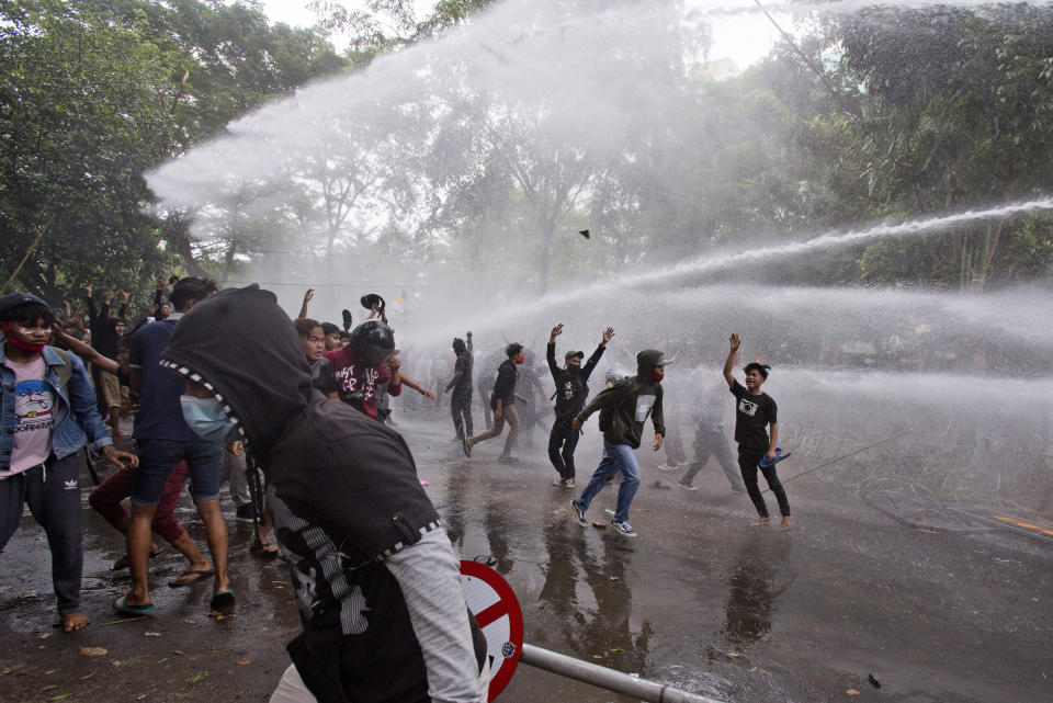 Protesters react as police use a water cannon to disperse them during a rally against a controversial bill on job creation in Medan, North Sumatra, Indonesia, Thursday, Oct. 8, 2020. Thousands of enraged students and workers staged rallies across Indonesia on Thursday in opposition to the new law they say will cripple labor rights and harm the environment. (AP Photo/Binsar Bakkara)