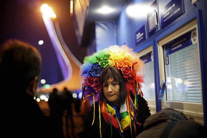 Vladimir Luxuria, a former Communist lawmaker in the Italian parliament and prominent crusader for transgender rights, waits to receive her ticket at a box office for a women's ice hockey match as the Olympic flame burns in the background at the 2014 Winter Olympics, Monday, Feb. 17, 2014, in Sochi, Russia. Luxuria was soon after detained by police upon entering the Shayba Arena to attend the women's ice hockey match. (AP Photo/David Goldman)