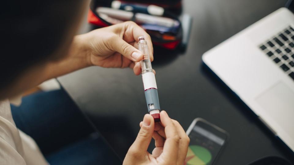 cropped image of businesswoman holding injection pen while sitting at office desk