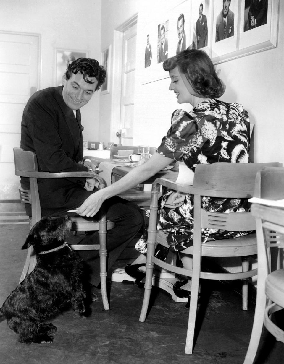 IN THIS OUR LIFE, from left, director John Huston, Bette Davis, feeding her dog, Tibby, in the Warner Brothers' commissary, 1942