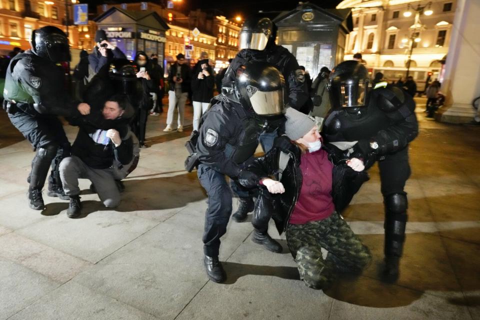 A woman, right, and a man are seized by security forces in black uniform and helmets