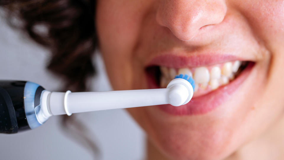 A young woman brushes her teeth with a black electric toothbrush - Image.