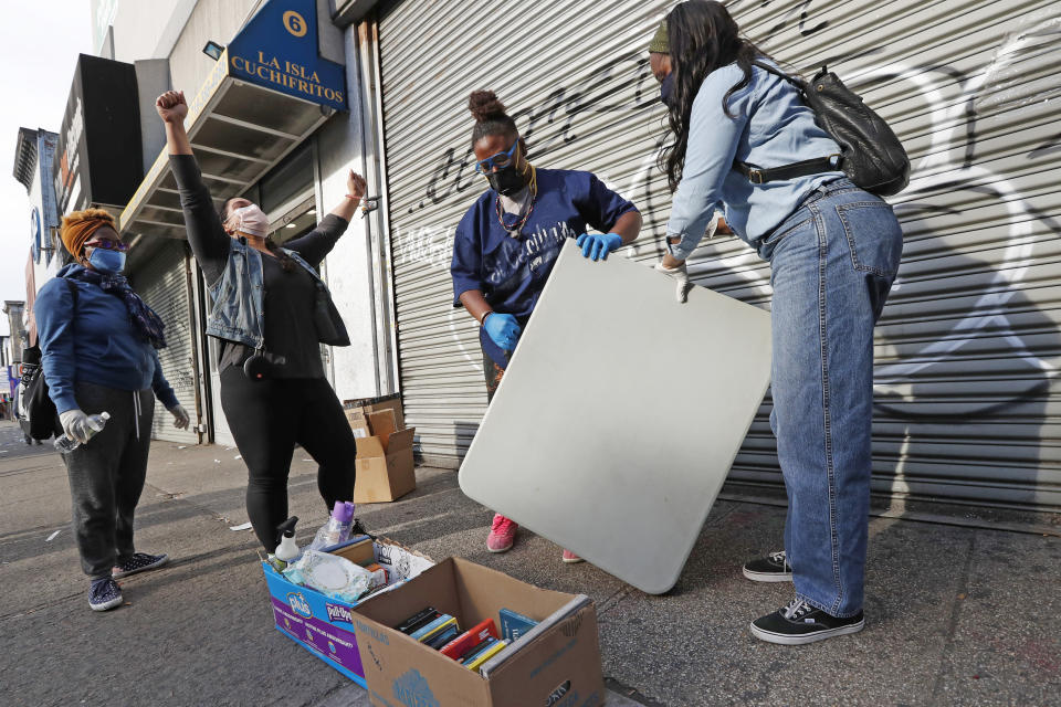 Sistas Van driver and Black Women's Blueprint employee Denise Rodriguez, second from left, celebrates after a day of giving back to her community by distributing free food, personal hygiene supplies, books, diapers and other items to anyone willing to wait in line to receive them from a mobile supply van amid the coronavirus outbreak, Tuesday, May 19, 2020, in New York. Volunteer Brooklyn Clayton, second from right, and Black Women's Blueprint intern Shabieko Ivy pack up the group's table as volunteer Marilyn Louis looks on, far left. Rodriguez dubbed the hard-working foursome her "dream team." (AP Photo/Kathy Willens)