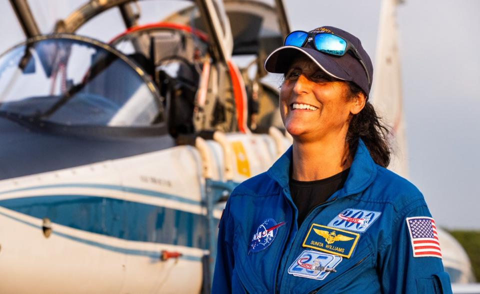 smiling female astronaut in a flight suit and hat in front of a jet aircraft, with open cockpit