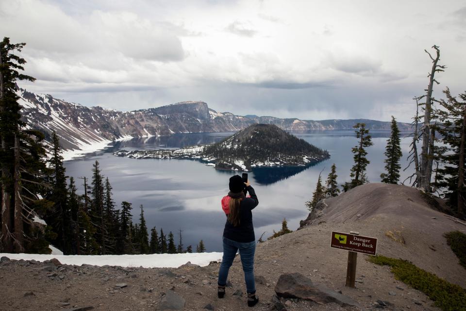 A person takes a photo of Crater Lake on June 1, 2023, in Crater Lake, Ore. Management issues at Oregon's Crater Lake have prompted the federal government to consider terminating its contract with the national park's concessionaire. Crater Lake Hospitality is a subsidiary of Philadelphia-based Aramark and is contracted through 2030 to run concessions such as food and lodging. (AP Photo/Jenny Kane)
