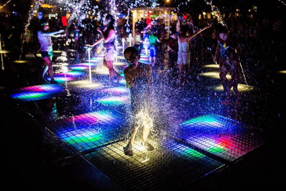 People play on an illuminated fountain at the Magic Water Circuit