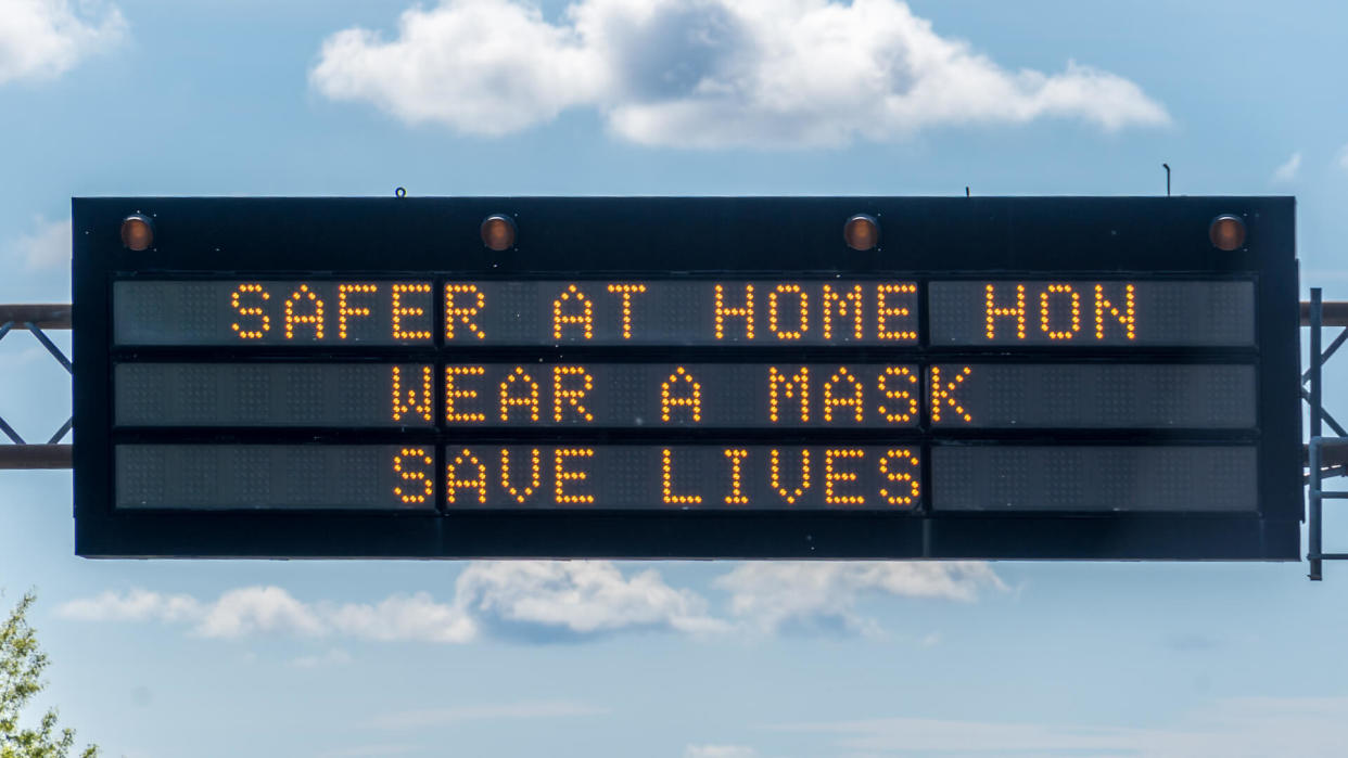 Safer at home, wear a mask sign over highway 32 in Maryland with a Baltimore "Hon" with cloudy blue sky.