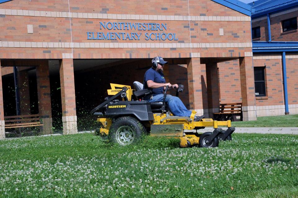 Northwestern Local Schools maintenance and grounds employee Eric Hall mows the grass in front of the elementary school building.