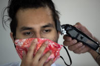 Agustin Aguilar holds his mask so barber Adrian Mayorga can cut his sideburns at the Country Club Barbers, Wednesday, May 27, 2020, in Escondido, Calif. Barber shops and hair salons were allowed to re-open, Wednesday in San Diego County, after closing to help stop the spread of the new coronavirus pandemic. (AP Photo/Gregory Bull)