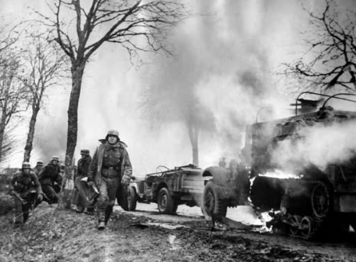 This photograph dated December 16, 1944, taken from a captured German's film, shows German infantrymen passing burning US Army vehicles somewhere on the Western Front