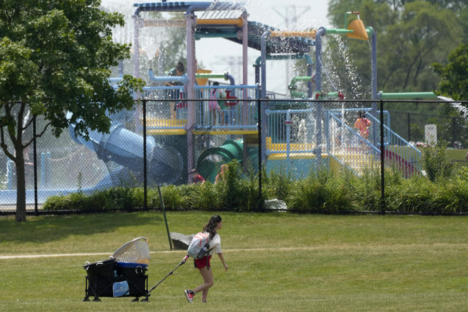 A woman carries wagon as she walks to Family Aquatic Center at Heritage Park during hot weather in Wheeling, Ill., Monday, June 17, 2024. (AP Photo/Nam Y. Huh)