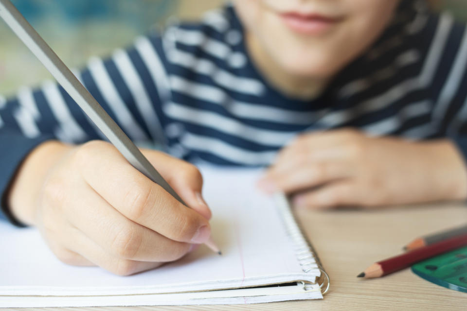 Kid writing in notebook and smiling. Close up.