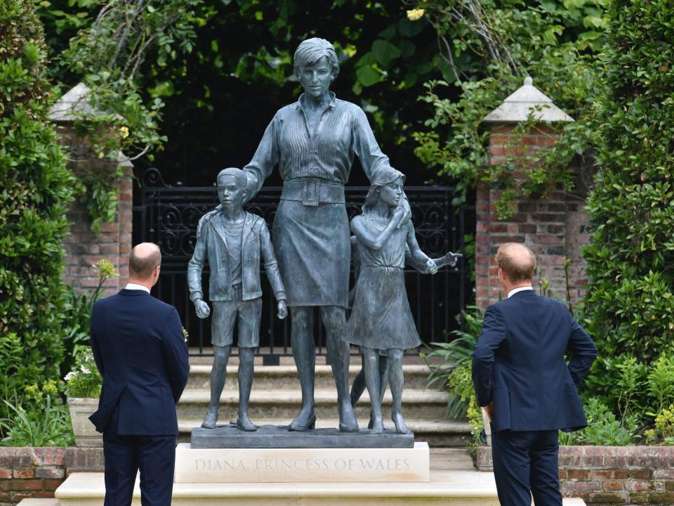 Prince William, left, and Prince Harry, right, look at a blue statue of Princess Diana surrounded by three children