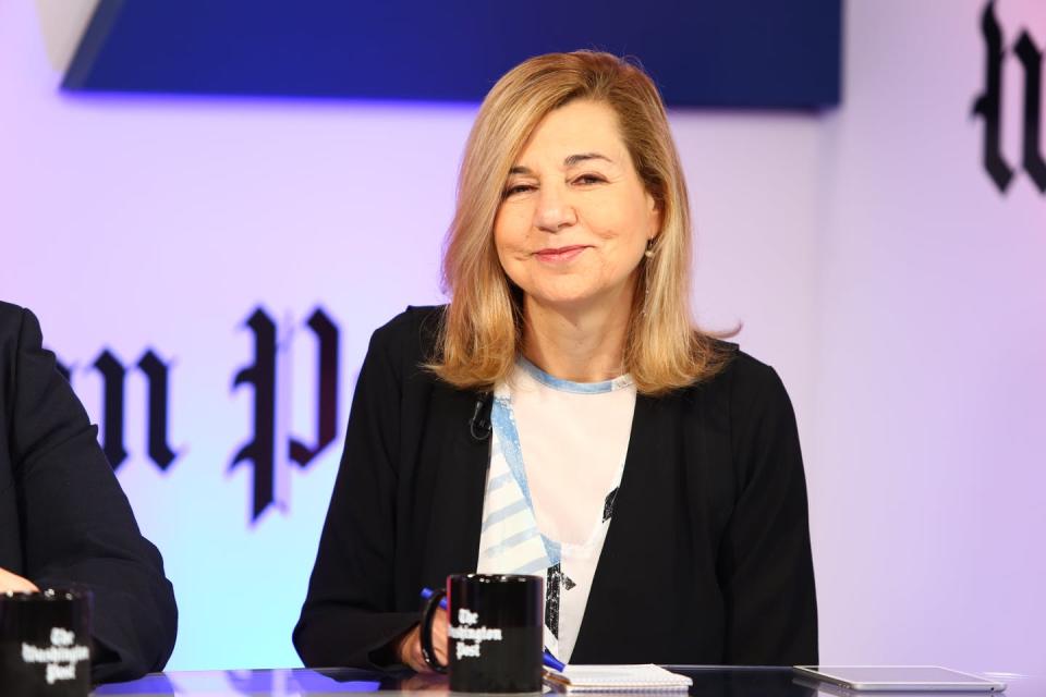 A middle-aged woman in white shirt, black sweater and with light brown hair.