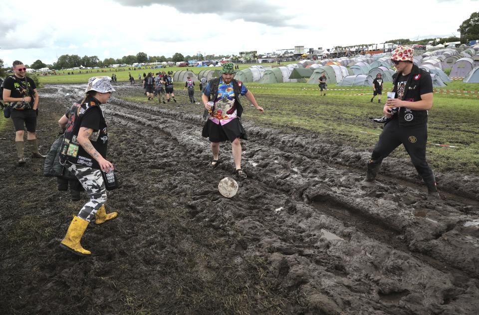 Metal fans play with a ball on the muddy festival grounds ahead of the beginning of the Wacken Open-Air (WOA) Festival, in Wacken, Germany, Tuesday Aug. 1, 2023. WOA Festival takes place from August 2 to August 5, and is considered the largest heavy metal festival in the world. (Christian Charisius/dpa via AP)