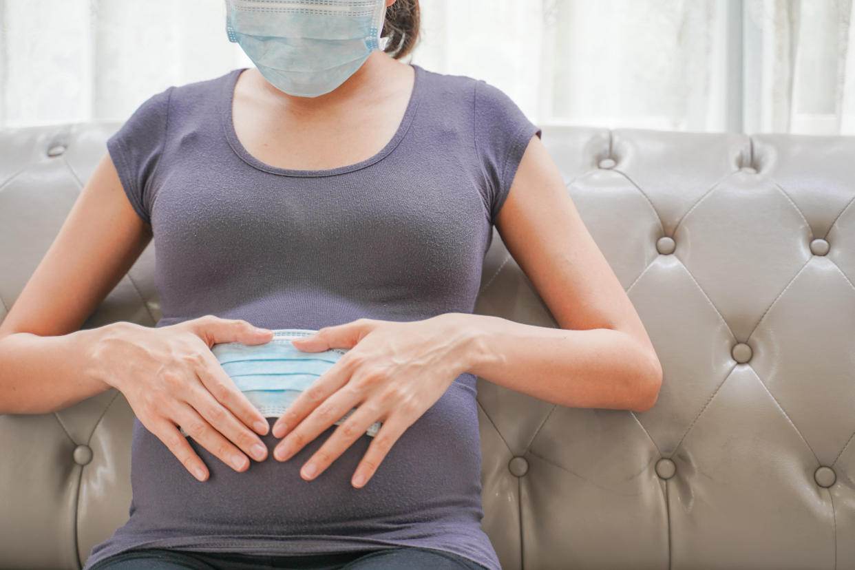 A pregnant woman wears a surgical mask to protect a COVID-19 (Coronavirus) and PM 2.5 and show a surgical mask on the abdomen to prevent infection to the fetus.