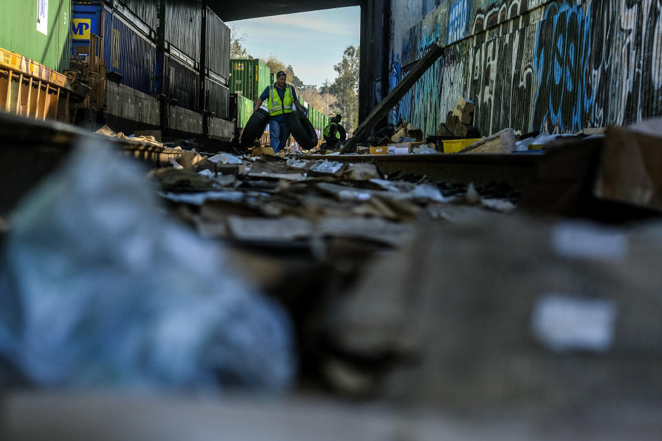 Contractor workers Adam Rodriguez, front, and Luis Rosas pick up vehicle tires from the shredded boxes and packages along a section of the Union Pacific train tracks in downtown Los Angeles Friday, Jan. 14, 2022. Thieves have been raiding cargo containers aboard trains nearing downtown Los Angeles for months, leaving the tracks blanketed with discarded packages. The sea of debris left behind included items that the thieves apparently didn't think were valuable enough to take, CBSLA reported Thursday. (AP Photo/Ringo H.W. Chiu)