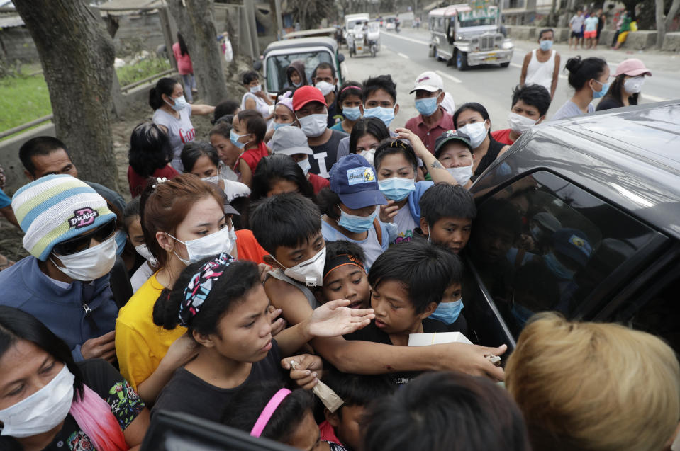 Residents scramble to grab relief goods given by a citizen at a town near Taal volcano, Tagaytay, Cavite province, southern Philippines on Sunday Jan.19, 2020. Many poor families living near Taal volcano have been affected due to loss of income after business closures in the area, Philippine officials said Sunday the government will no longer allow villagers to return to a crater-studded island where an erupting Taal volcano lies, warning that living there would be "like having a gun pointed at you." (AP Photo/Aaron Favila)