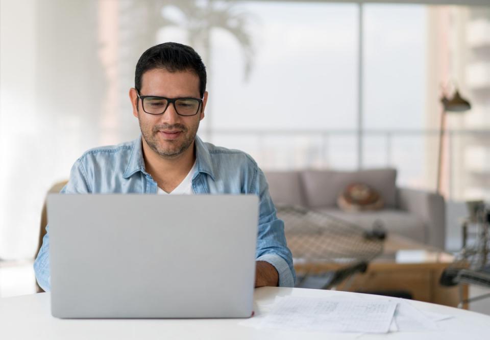 A person smiling while sitting at a table with a laptop computer. 