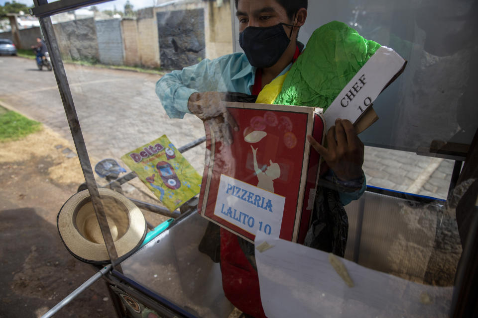Standing behind the plexiglass window of his mobile classroom, Gerardo Ixcoy holds a pizza box as part of a lesson on fractions, in Santa Cruz del Quiche, Guatemala, Wednesday, July 15, 2020. "I tried to get the kids their work sheets sending instructions via WhatsApp, but they didn't respond," Ixcoy said. "The parents told me that didn't have money to buy data packages (for their phones) and others couldn't help their children understand the instructions." (AP Photo/Moises Castillo)