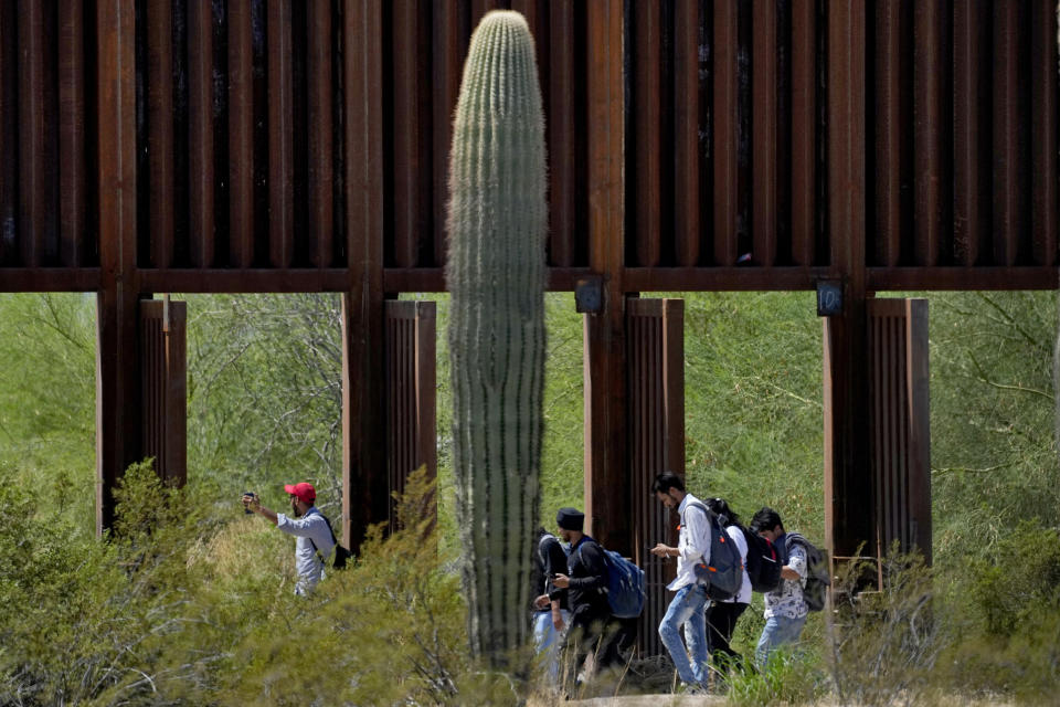 A group claiming to be from India walk past open border wall storm gates after crossing through the border fence in the Tucson Sector of the U.S.-Mexico border, Tuesday, Aug. 29, 2023, in Organ Pipe Cactus National Monument near Lukeville, Ariz. Migrants walk through storm gates currently open in the towering wall of steel bollards due to possible rains during the monsoon season that ends in two weeks. There were several heavy downpours in the area this year and CBP said rushing water can damage the gates, wall, border road, and local flora and fauna. (AP Photo/Matt York)