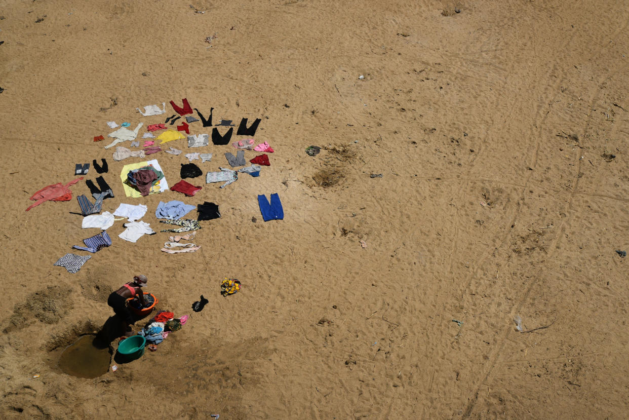 A woman, next to clothes laid out on the ground, does her laundry in a hole dug to access water in the village of Tsihombe.