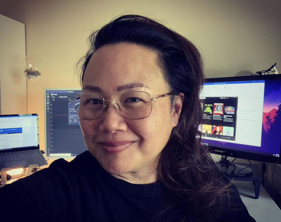 Woman smiling with glasses, in front of computer monitors, indoors