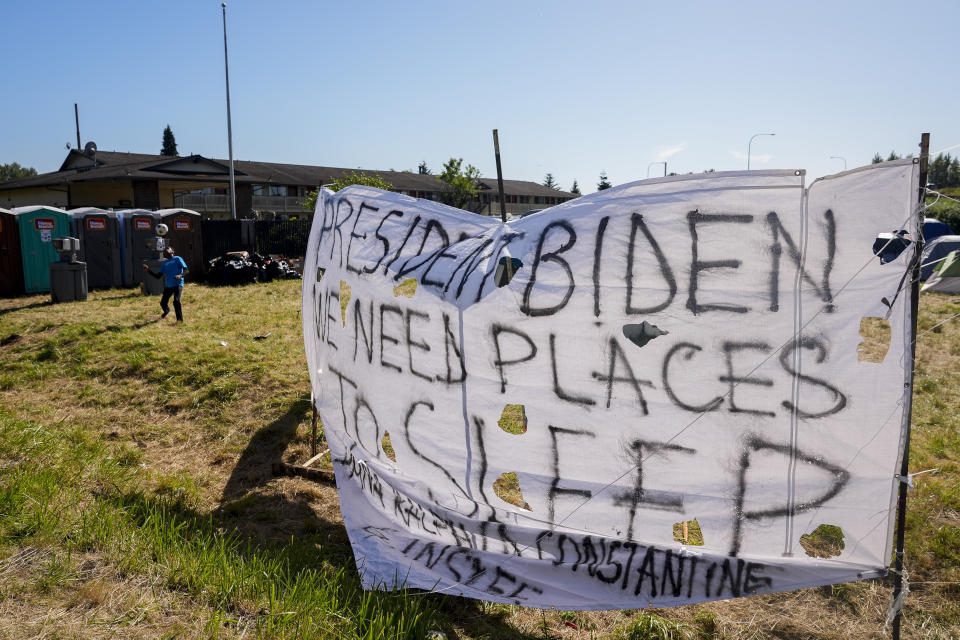 A sign hangs in front of an encampment of asylum-seekers mostly from Venezuela, Congo and Angola next to an unused motel owned by the county, Wednesday, June 5, 2024, in Kent, Washington. The group of about 240 asylum-seekers is asking to use the motel as temporary housing while they look for jobs and longer-term accommodations. (AP Photo/Lindsey Wasson)
