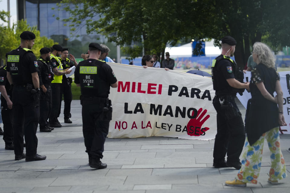 Demonstrators show banners and posers as they protest against the visit of Argentina's President Javier Milei for a meeting at the chancellery to meet German Chancellor Olaf Scholz in Berlin, Germany, Sunday, June 23, 2024. Banner reads: Milei for the hand, no to the base law. (AP Photo/Markus Schreiber)