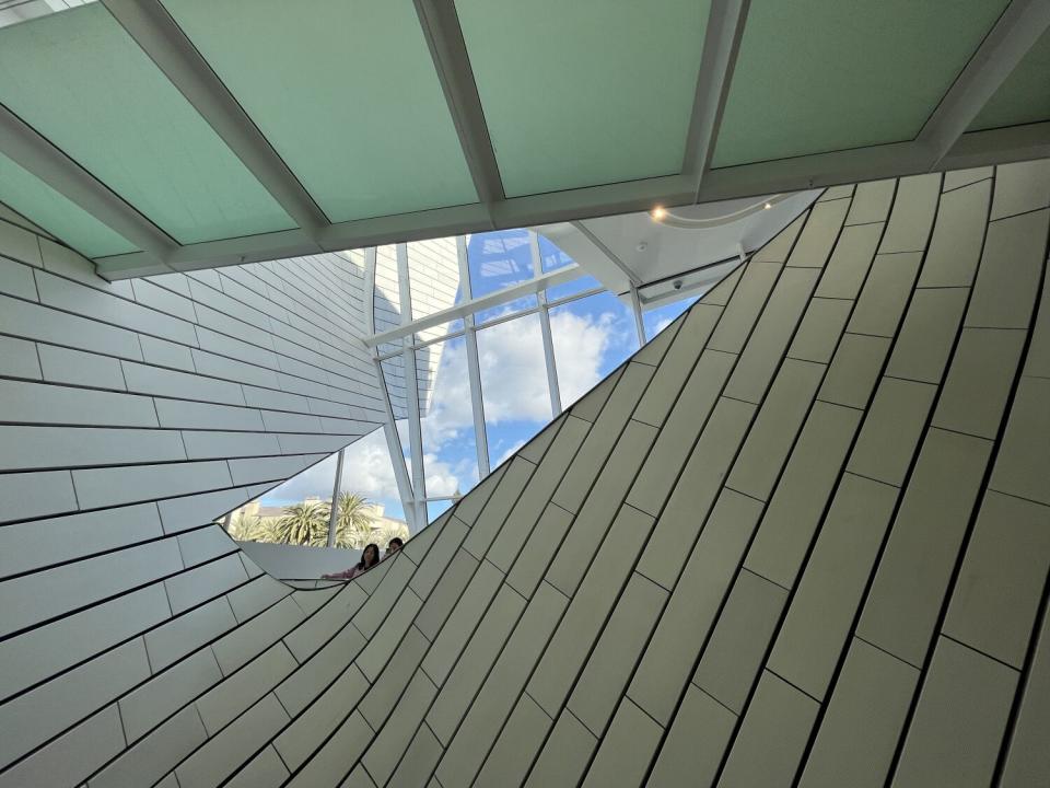 An upwards view shows an undulating atrium wrapped in white terra-cotta tile with a sliver of sky in the distance