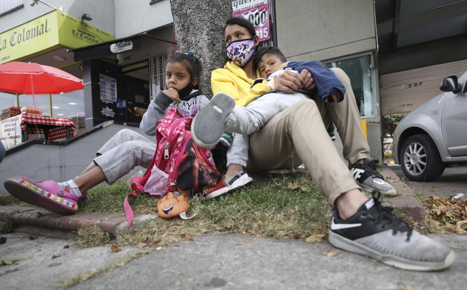 Venezuelan migrant Katerine Valero, 29, and her children Dariusca, 8, left, and Wilkerson, 4, rest outside a strip mall, in Bogota, Colombia, Tuesday, Feb. 9, 2021. Colombia said Monday it will register hundreds of thousands of Venezuelan migrants and refugees currently in the country without papers, in a bid to provide them with legal residence permits and facilitate their access to health care and legal employment opportunities. (AP Photo/Fernando Vergara)